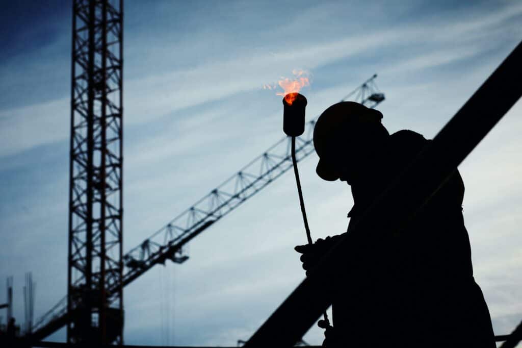 高空施工工人 silhouetted against construction crane and sky, highlighting global labor workforce.