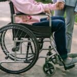 輪椅上的殘障人士與陪伴者手牽手的溫馨畫面，展現人道關懷與社會包容。.