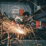 高雄工業廠房焊接作業現場，工人穿戴安全裝備進行金屬焊接，產生火花與閃光，展現專業技術與工廠生產力。.