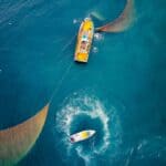 貨櫃船與快艇航行於海面上，展現21世紀全球外勞集團的國際合作與海上物流實力。.