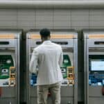 自動售票機旁等待乘客的男子，展示都市交通與外勞就業相關場景。.