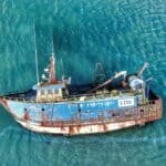 廢棄老舊漁船沉沒在海面上，象徵漁業資源枯竭與環境保護議題。.