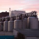 高架工業製造廠房的金屬儲存罐，夕陽映照下的工業景觀，展示21世紀全球外勞集團的工業背景。.