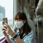 穿著口罩的年輕女性在地鐵上使用手機，彰顯都市通勤生活與科技便利。.