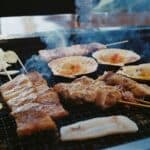 燒烤食材在烤架上炙烤，包括肉串和海鮮，氛圍熱鬧美味；適合戶外燒烤聚餐。.