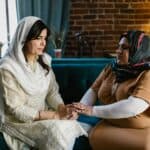 悲傷中兩位女性握手安慰，代表跨文化支援與理解，展現全球外勞的重要價值。.