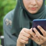 手機使用中的亞洲女性，專注於手機屏幕，展現科技在全球外勞行業的重要性。.