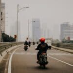 騎摩托車的外勞穿梭於都會高樓林立的繁忙城市道路中，展現全球外勞在亞洲城市的重要角色與經濟貢獻。.