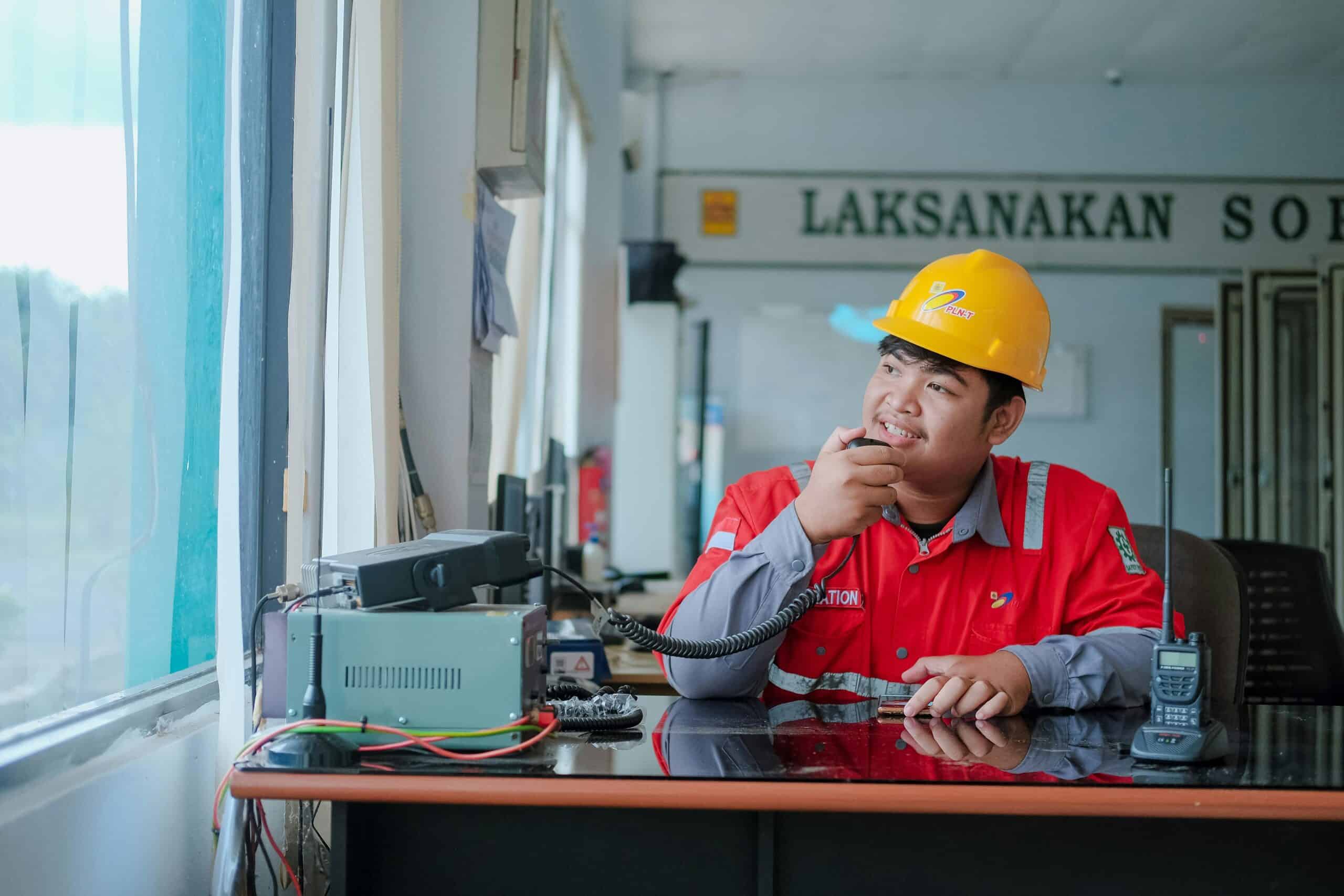 外籍移工|預防感電等職業危害 894 家企業申請  重建中心提供免費輔導與教育訓練 高雄外勞管理員在辦公室操作通訊設備,展現外籍勞工管理與溝通服務專業形象.