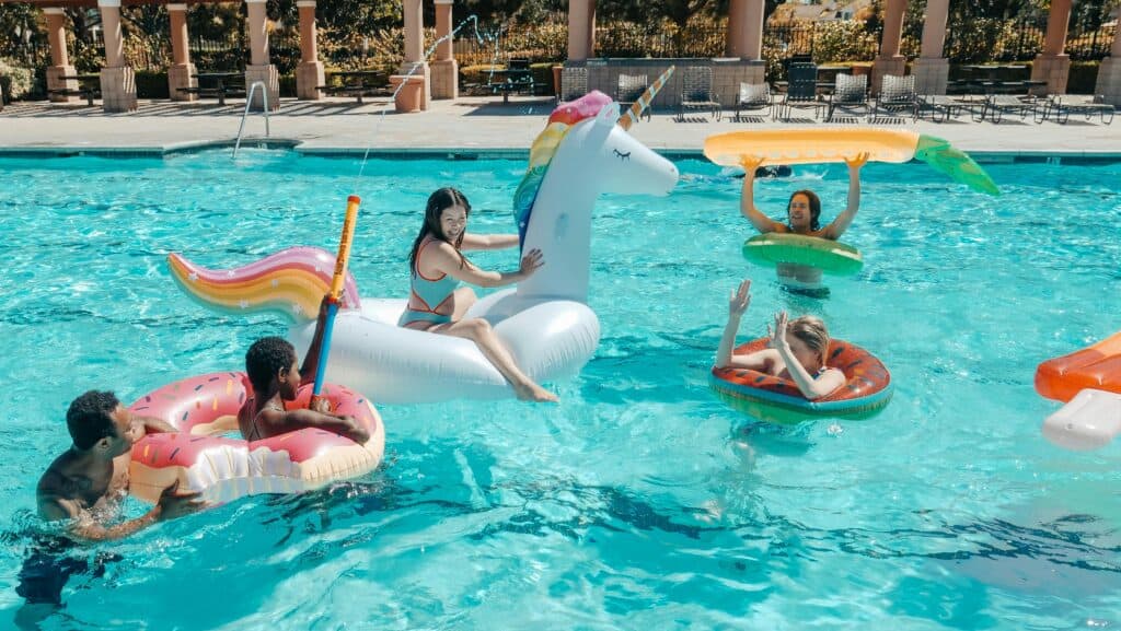 彩色獨角獸浮圈和多彩泳圈中的多國外勞在游泳池休閒娛樂.