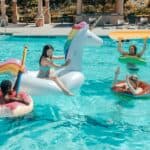 彩色獨角獸浮圈和多彩泳圈中的多國外勞在游泳池休閒娛樂.